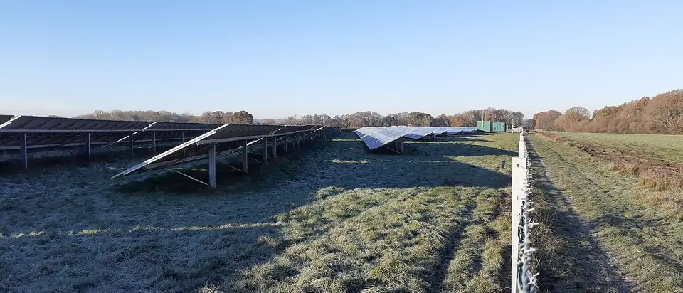 Rows of solar panels on frosty grass on a clear morning at Chalcroft Solar Park, England.